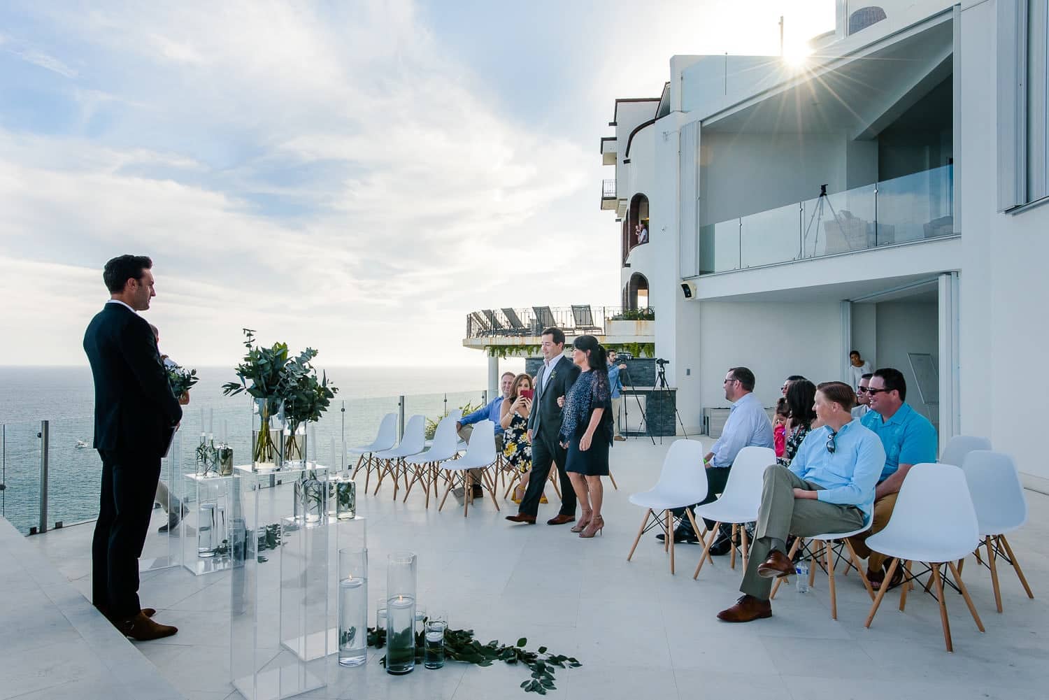 Villa Lands End cabo wedding ceremony in progress on the Pedregal cliff terrace — guests in white chairs, aisle, officiant, and the Pacific Ocean