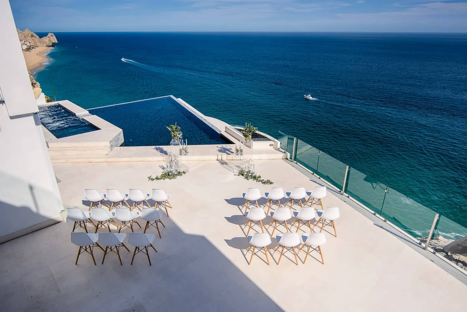Villa Lands End cabo wedding ceremony setup in Pedregal: twenty-four white chairs, lucite pedestals, greenery, triangular infinity pool, and the Pacific