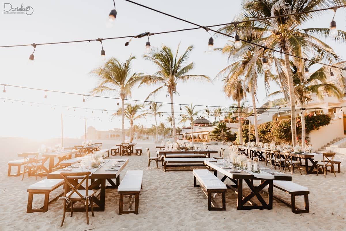 Golden-hour cabo wedding dinner on Pedregal beach — long tables on the sand, festoon lights, candles