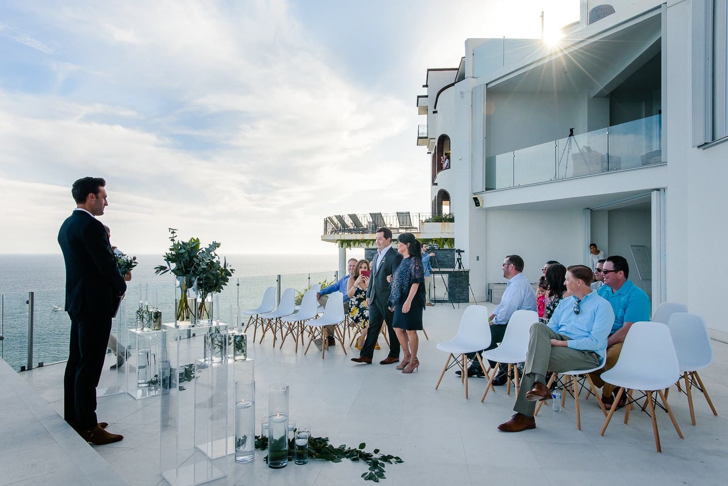 Villa Lands End cabo wedding ceremony in progress on the Pedregal cliff terrace — guests in white chairs, aisle, officiant, and the Pacific Ocean